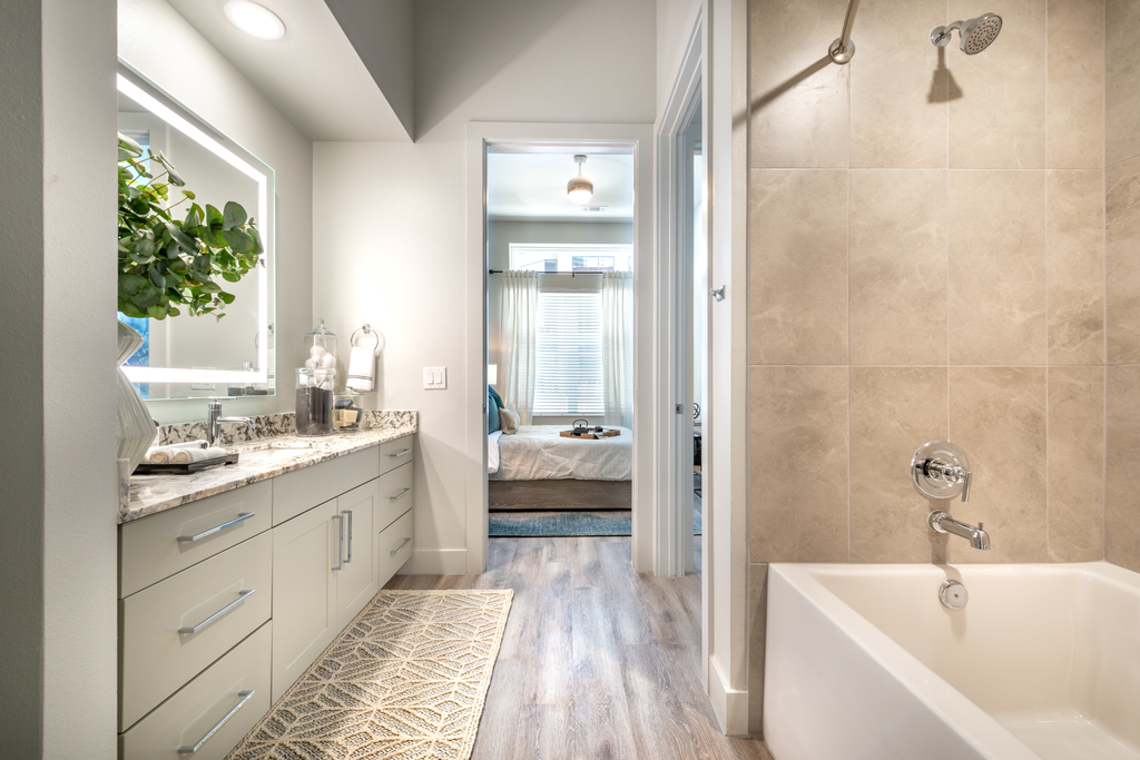 Staged bathroom with wood style flooring, garden tub, granite countertop, white cabinetry and custom lighted vanity mirror