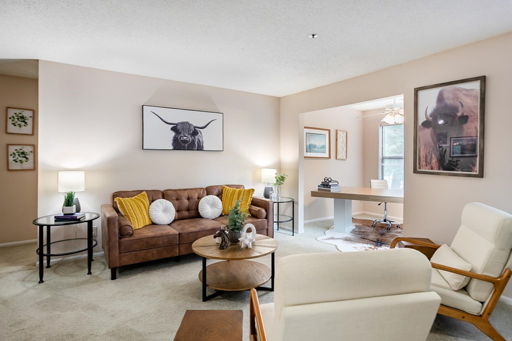 A living room with a brown couch, a white chair, and a painting of a bull on the wall.
