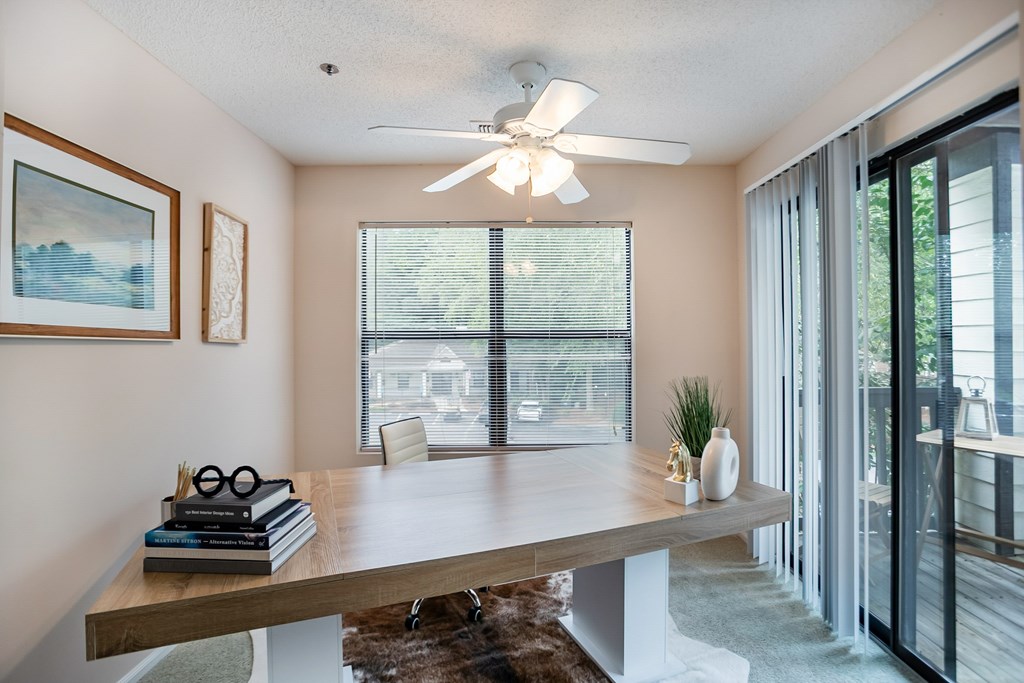 A room with a ceiling fan and a table with a vase and books on it.