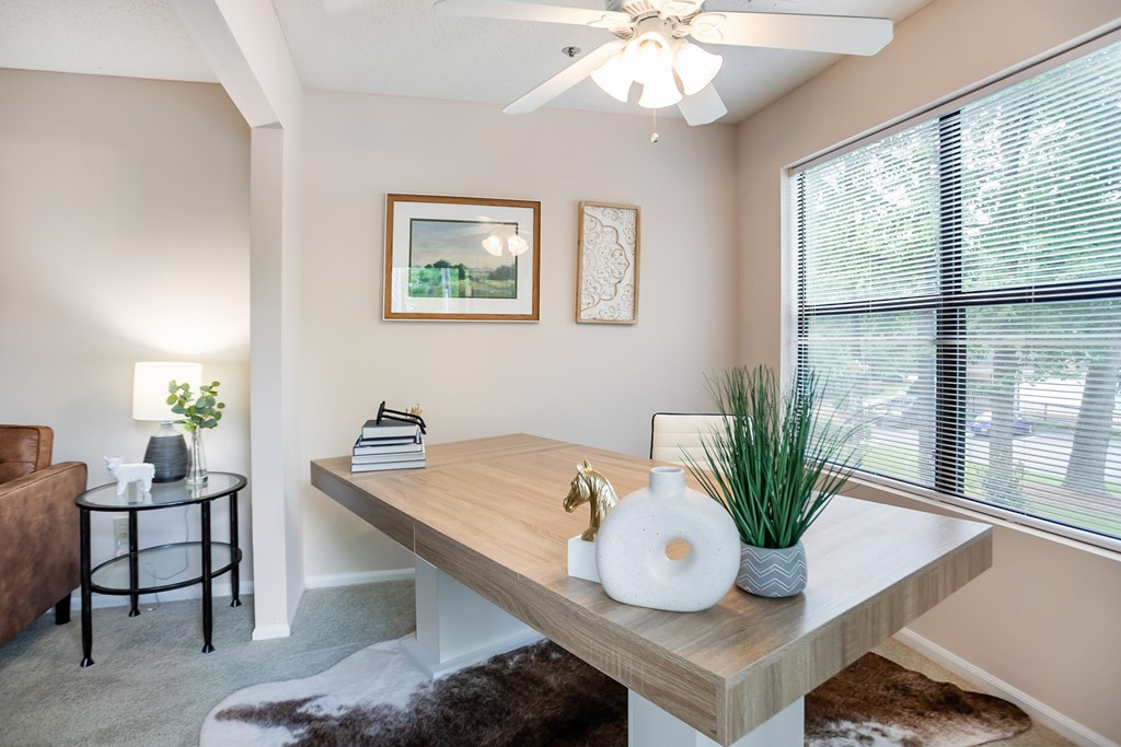 A room with a table, a chair, a ceiling fan, and a window.