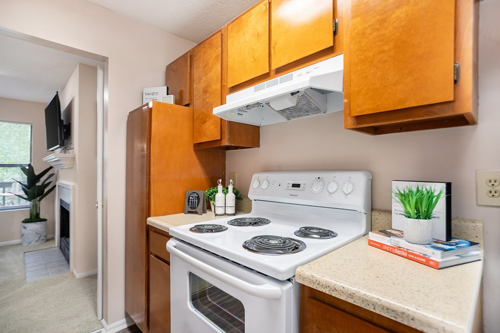 A kitchen with a white stove top oven and wooden cabinets.