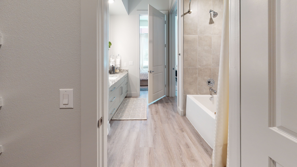 Staged bathroom with wood style flooring, garden tub, bathroom mat, granite countertops, and direct access from bedroom
