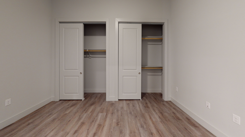 Bedroom with wood style flooring and two closets with shelves and rack