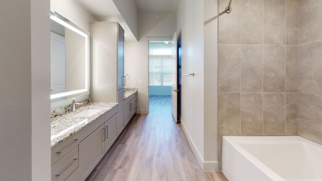 Bathroom with garden tub, wood style flooring, granite countertops, dual vanities, custom vanity mirror and taupe cabinetry