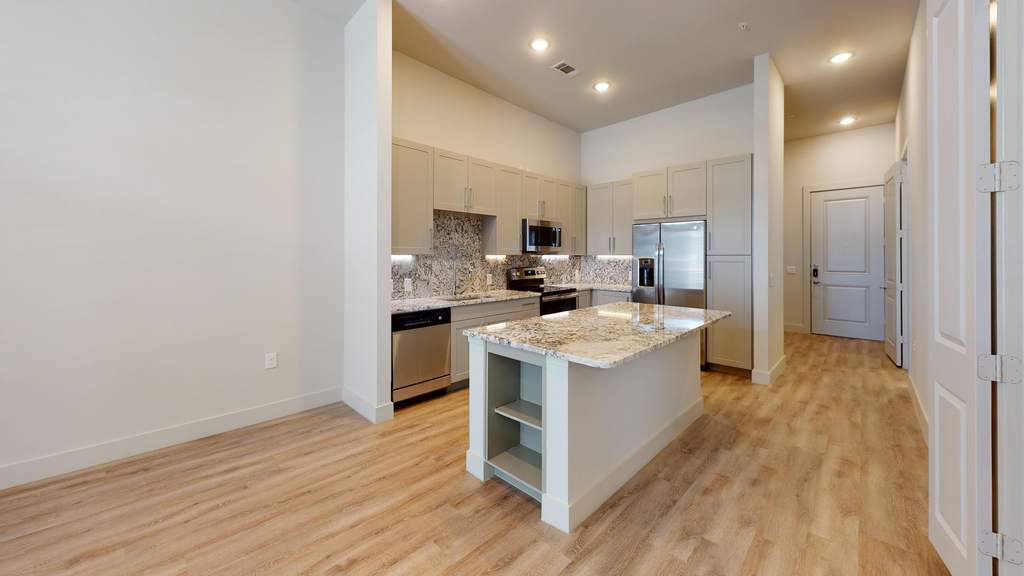 Kitchen with kitchen island, granite countertops,. wood style flooring, stainless appliances, taupe cabinetry, and wood style flooring