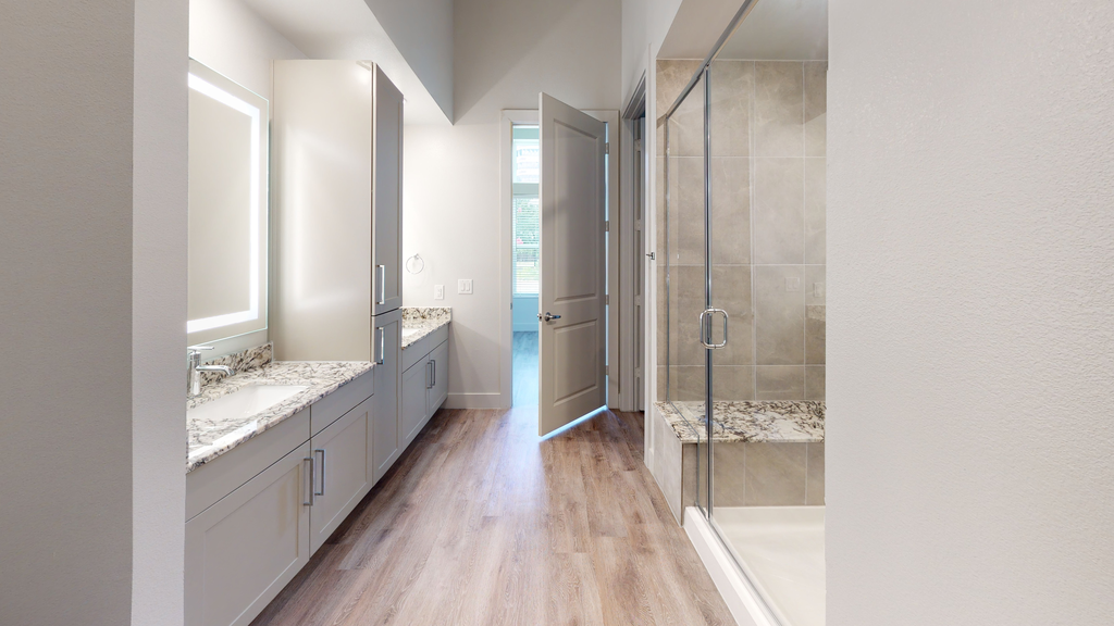 Bathroom with wood style flooring, walk in shower with granite bench, granite countertops, dual vanities, custom vanity mirror and taupe cabinetry