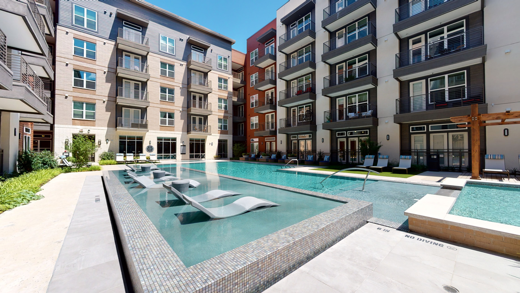Swimming pool with tanning shelf and lounge chairs with building exterior surrounding