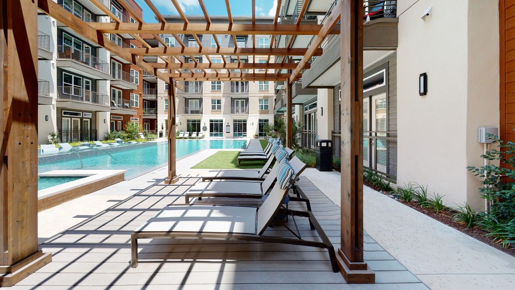 Lounge chairs poolside with pergolas, deck, fountains, and native landscape with building exterior surrounding