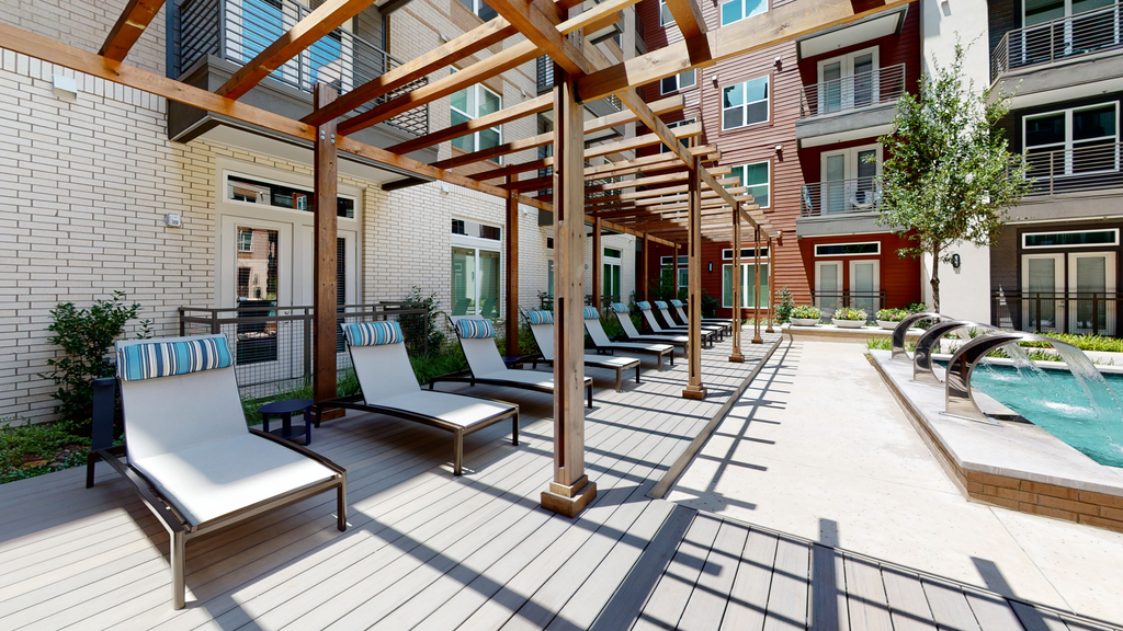 Lounge chairs poolside with pergolas, deck, fountains, and native landscape with building exterior surrounding