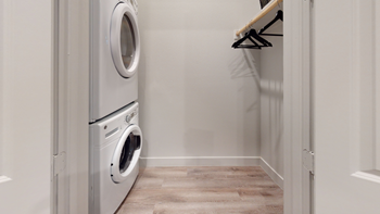 Staged laundry room with stacked front loading washer and dryer with clothes rack and shelf