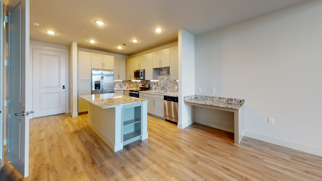 Kitchen with wood style flooring, kitchen island, granite countertops, built in desk, stainless appliances, recessed lighting, shaker cabinetry