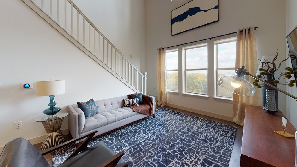 Living room area facing a couch and television next to an exterior window and staircase