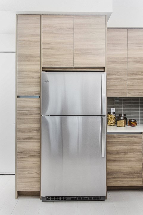 A stainless steel refrigerator in a modern kitchen with wooden cabinets.