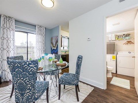 Furnished Model Dining Room with Glass Dining Table and Chairs on Area Rug Next to Utility CLoset with Washer and Dryer