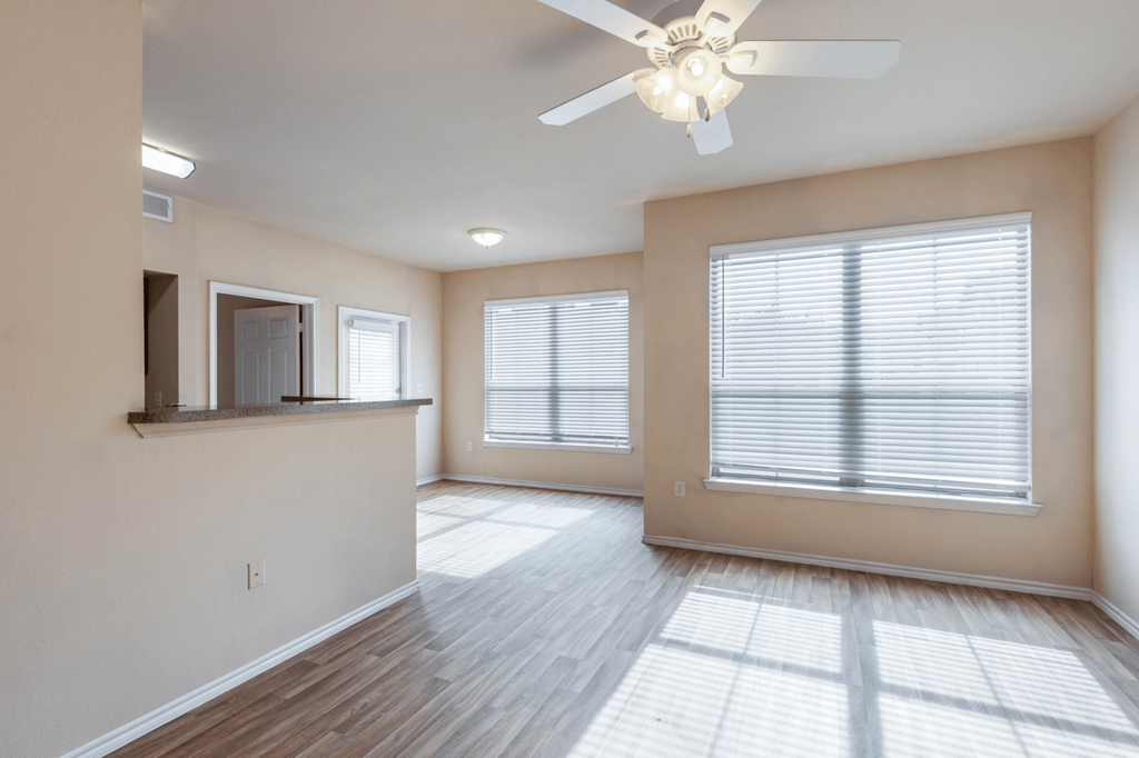 a living room with two windows and a ceiling fan. The room opens up to the dining room and kitchen breakfast bar.