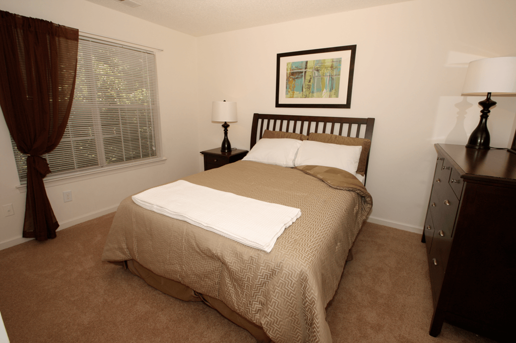 Bedroom with queen size bed, nightstand, dresser and large window.