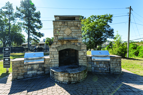 A stone fireplace with a grill on top is in the middle of a brick patio.