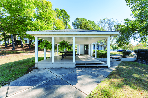 A covered porch area with a white house and a black car in the background.