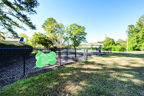 A dog park sign is on a fence in a grassy area.