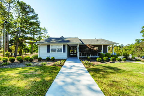 A white house with a grey roof and a long concrete pathway leading to the front door.