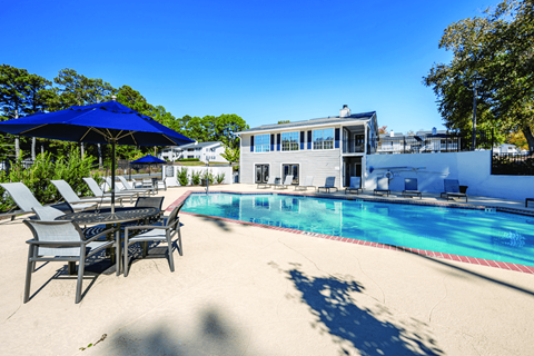 A pool with chairs and umbrellas in front of a house.