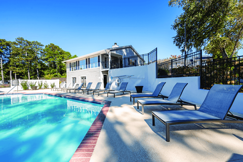 A pool with blue water and sun loungers in front of a white building.