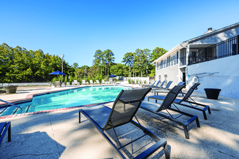 A pool with chairs around it and a building in the background.
