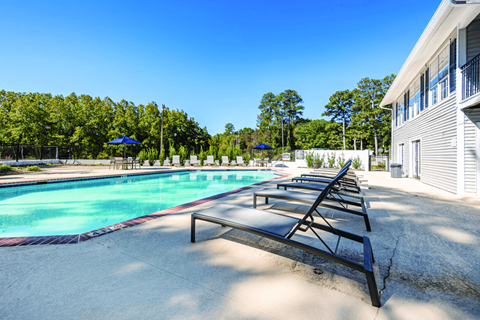 A pool with sun loungers and a building in the background.