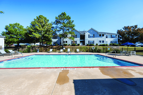 A swimming pool in front of a white building with trees in the background.