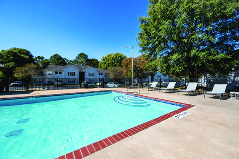 A swimming pool surrounded by chairs and trees.