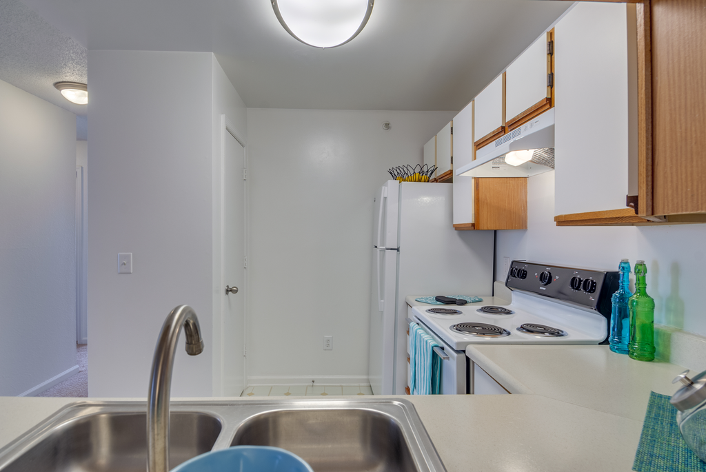 The three bedroom kitchen has white cabinets with tan trim, white appliances, formica countertops, and a double basin sink with gooseneck faucet.