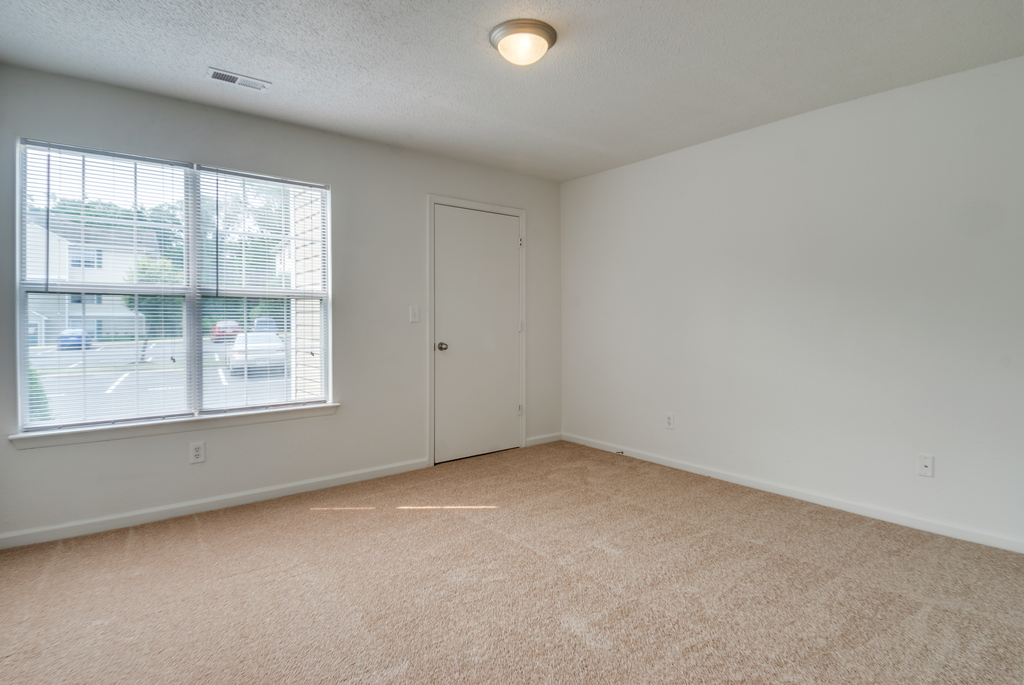The vacant bedroom has wall to wall carpet, a large picture window and a door leading to a closet.
