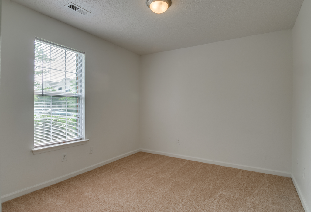 The vacant bedroom has wall to wall carpet, white walls and a standard window on one of the walls.