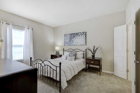 A bedroom with a bed, nightstand, and a painting on the wall.