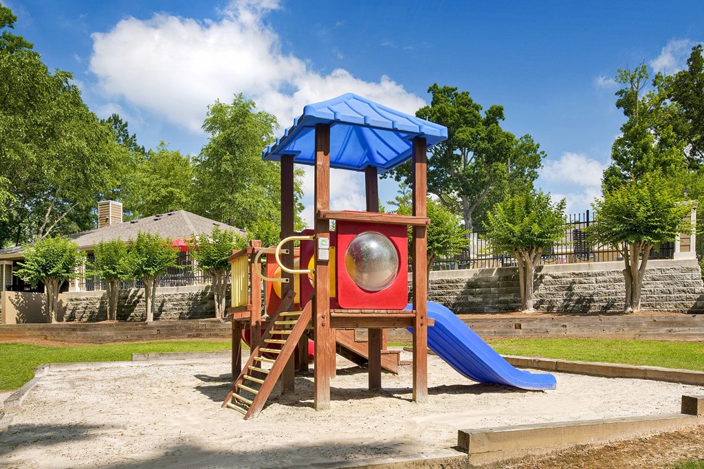A playground with a blue umbrella and a red slide.