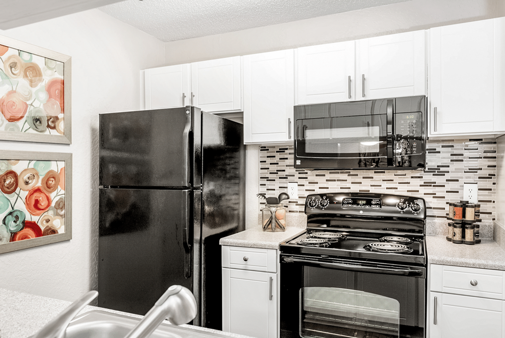 A black refrigerator stands in a kitchen with white cabinets and a black stove at Paces Pointe Apartment Homes, Matthews