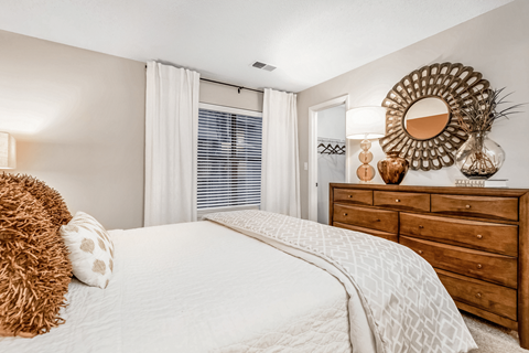 A bedroom with a large bed, a wooden dresser, and a mirror on the wall.