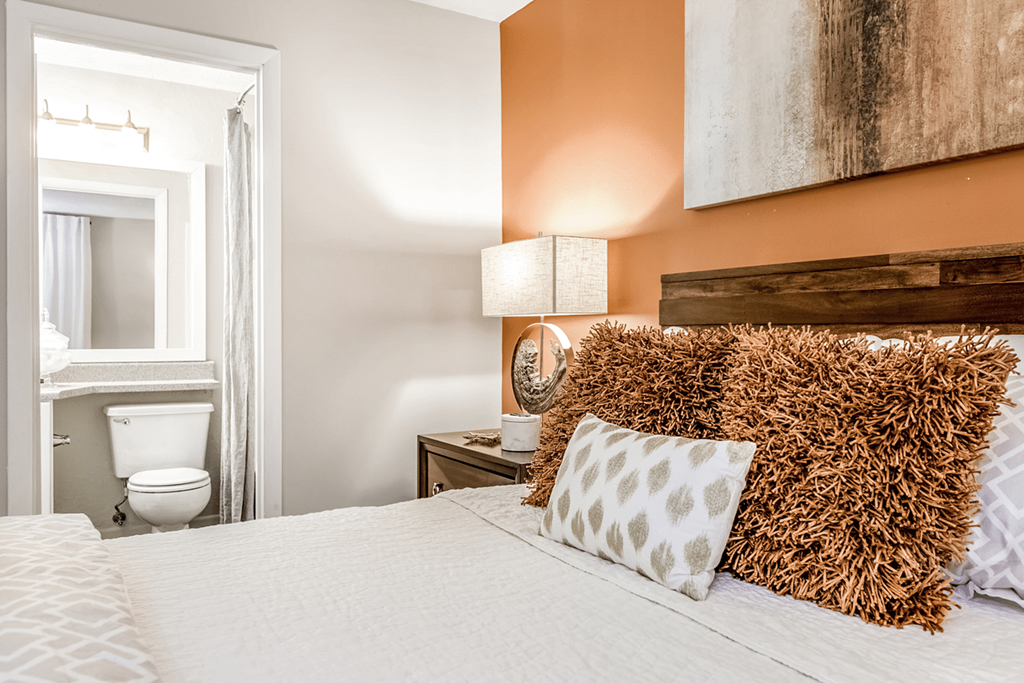 A bedroom with a large bed, a nightstand with a lamp, and a painting on the wall at Paces Pointe Apartment Homes, Matthews, NC