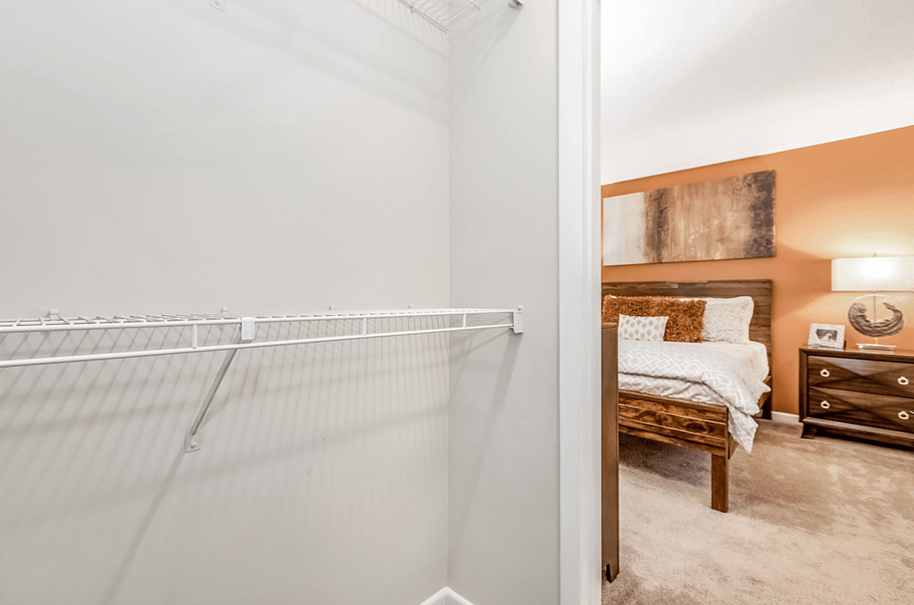 A white bedroom with a bed, nightstand, and a wall hanging at Paces Pointe Apartment Homes, Matthews, 28105