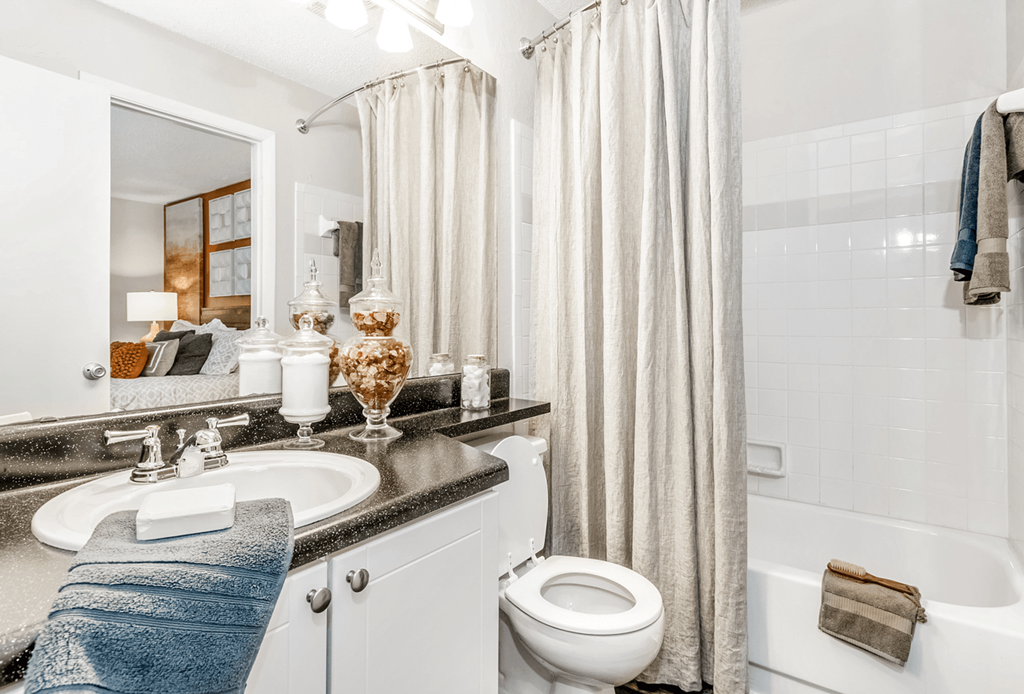 A bathroom with a white toilet, a sink, a bathtub, and a shower curtain at Paces Pointe Apartment Homes, North Carolina