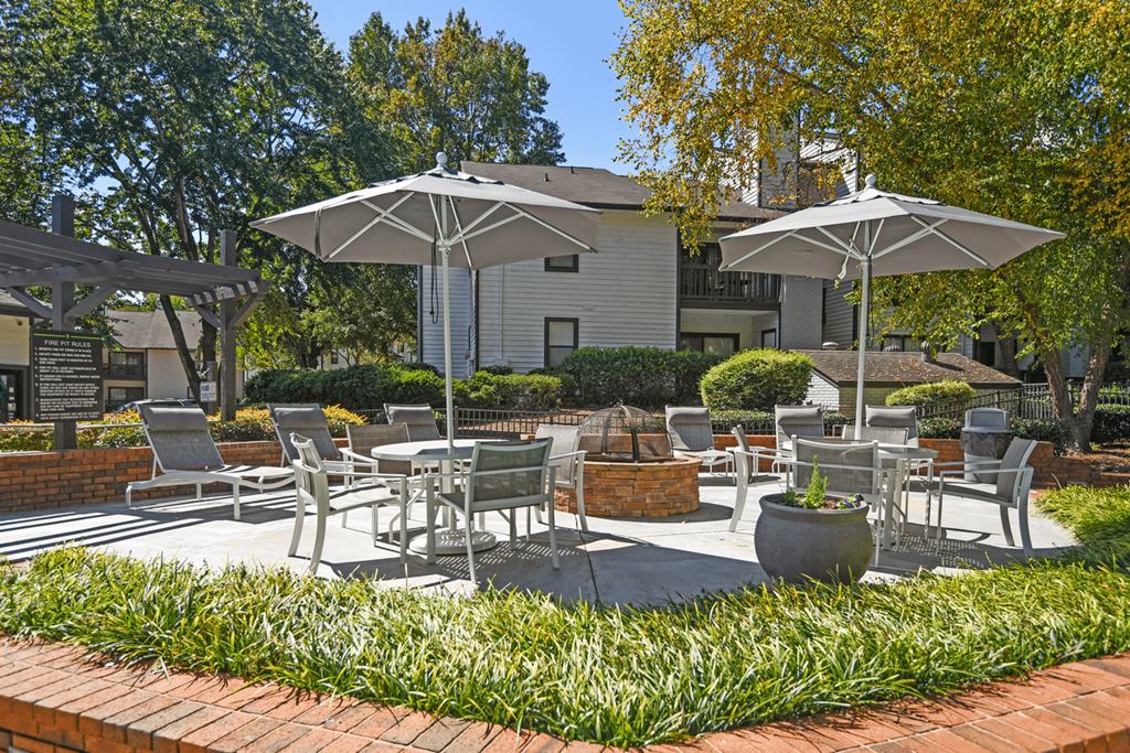 A patio with chairs and umbrellas is surrounded by green plants at Paces Pointe Apartment Homes, North Carolina, 28105