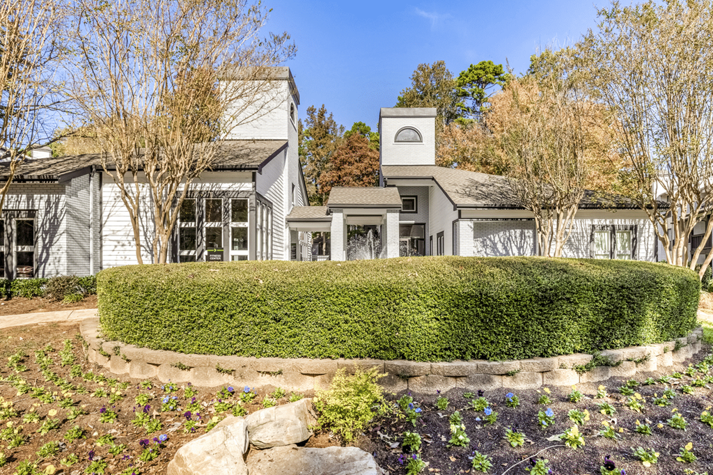 A white house with a grey roof and a small tower is surrounded by a well-manicured garden at Paces Pointe Apartment Homes, North Carolina