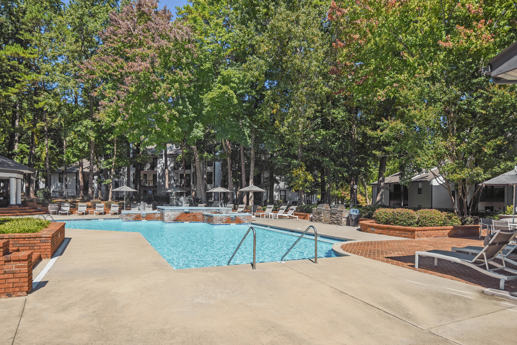 A swimming pool surrounded by trees and umbrellas at Paces Pointe Apartment Homes, Matthews, 28105