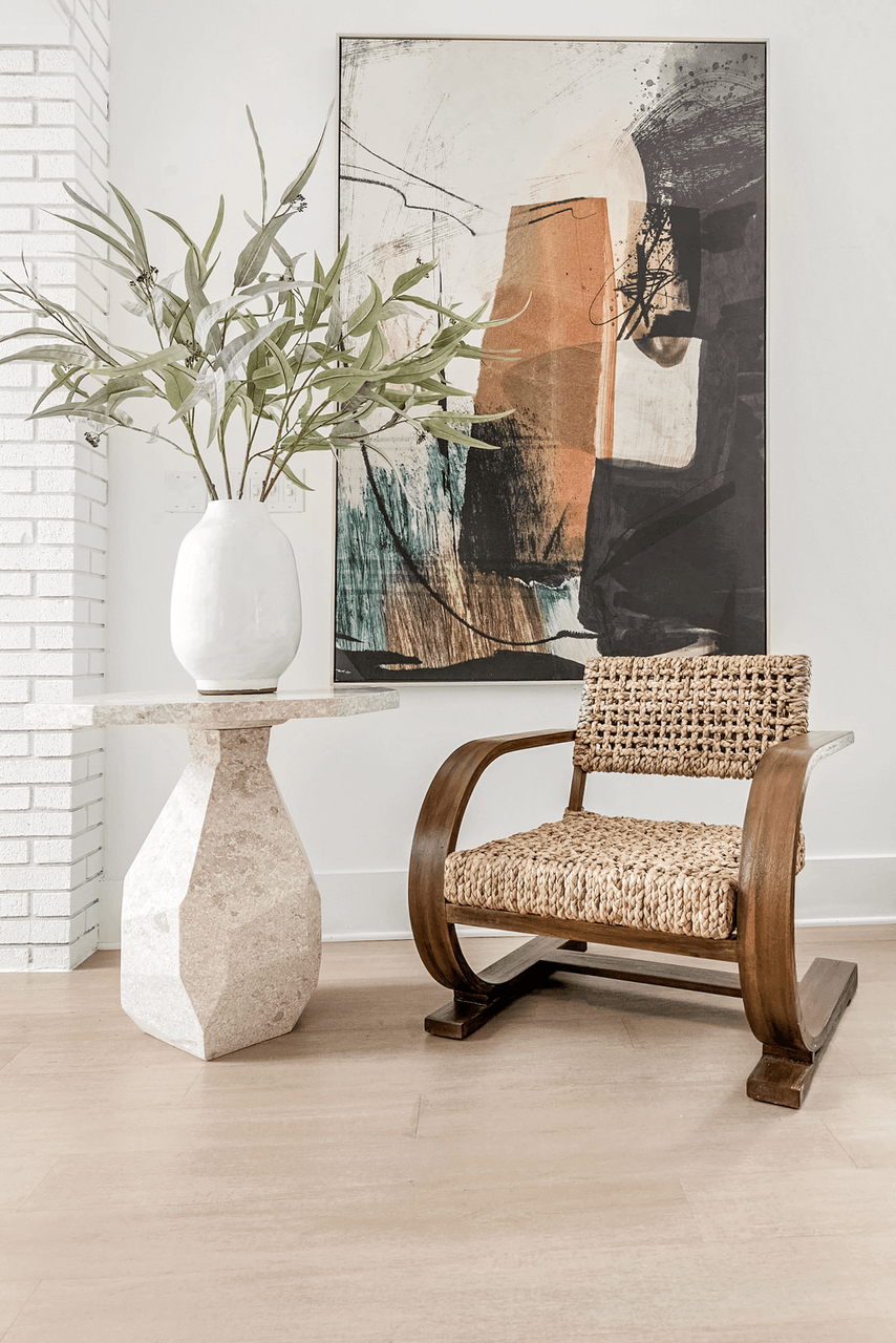 A chair with a woven seat and a white vase with a plant sits in front of a painting at Paces Pointe Apartment Homes, North Carolina, 28105