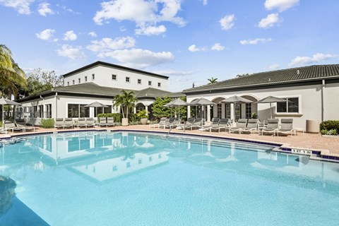 a swimming pool with lounge chairs and umbrellas in front of a white building