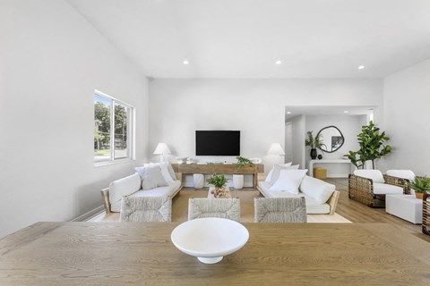 A modern living room with a white sofa set, a wooden coffee table, and a flat-screen TV.