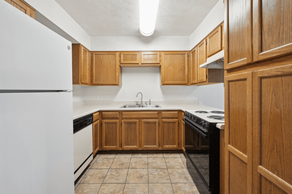 an empty kitchen with wooden cabinets and a white refrigerator at Patriot Point Apartment Homes, Spring Lake, NC 