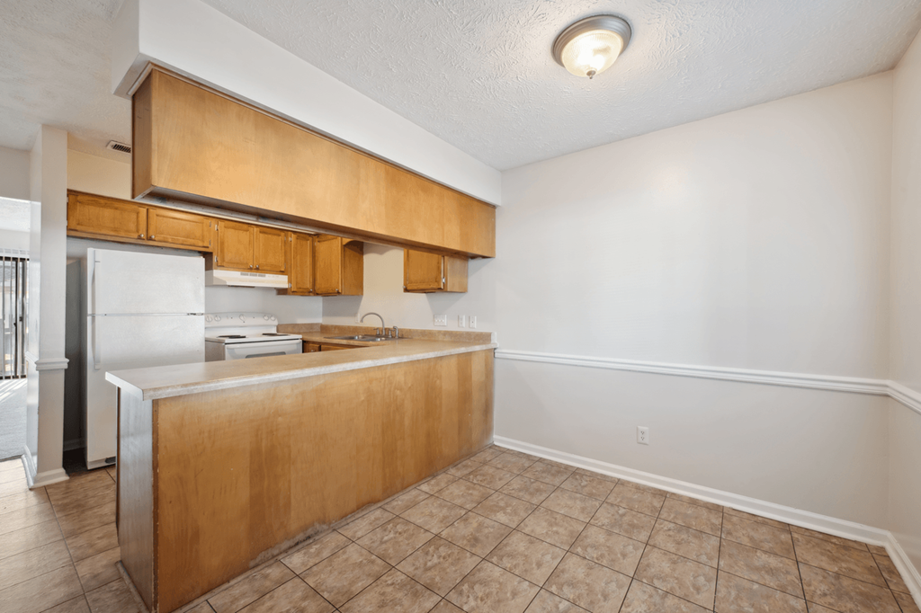 an empty kitchen with wooden cabinets and a white refrigerator at Patriot Point Apartment Homes, Spring Lake, NC 
