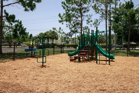 Playground jungle gym and playground slides in a bed of mulch with trees in the background