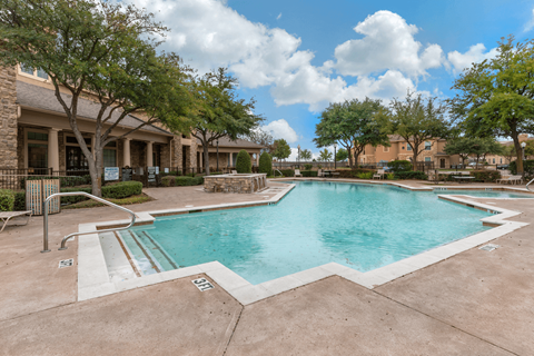 A large outdoor swimming pool surrounded by trees and a building.